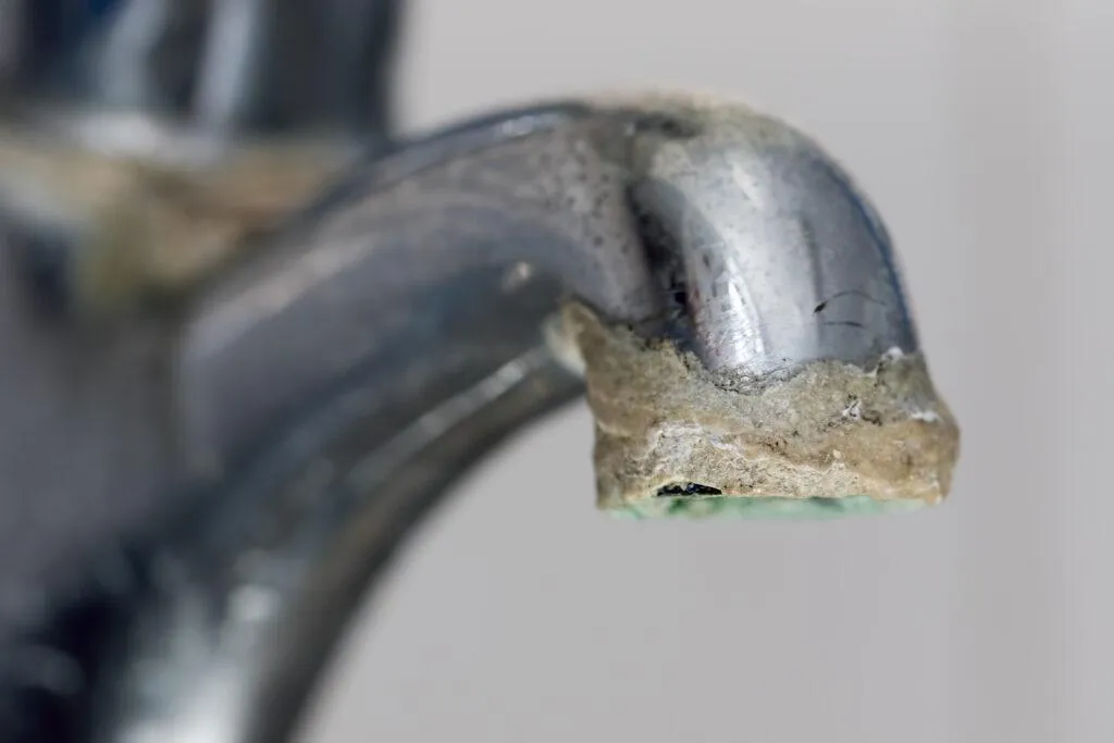 White limescale residue crust around a tap and inside a kettle in Tenerife — caused by high mineral content in desalinated tap water